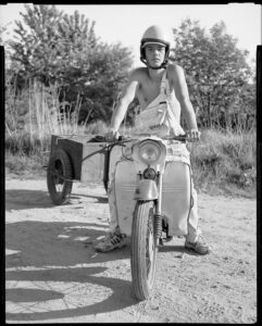 Czarno-biała fotografia. Męrzczyzna jadący na motorze z przyczepką.