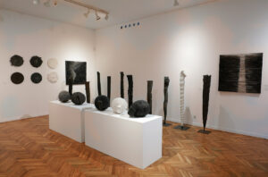 Część ekspozycji przedstawiająca prace ceramiczne wiszące na ścianach w kształcie obrazów oraz stojące w kształcie talerzy, kul i obelisków