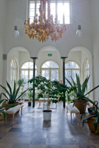 sala z dwoma kolumnami podtrzymującymi sklepienie łukowe, wypełniona stojącymi dużymi roślinami