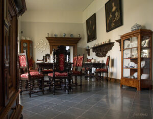 sala z krzesłami i stołem, obok szafka z porcelanowymi naczyniami, na ścianach wiszą obrazy