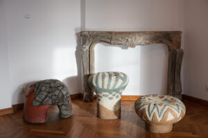 Trzy wolno stojące figury ceramiczne w kształcie siedzisk na tle kamiennego kominka