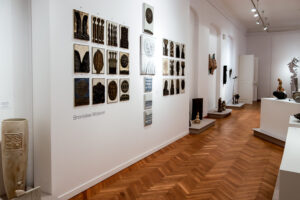 Część ekspozycji przedstawiająca wiszące na ścianie obrazy ceramiczne z elementami roślinnymi autorstwa Bronisława Wolanina
