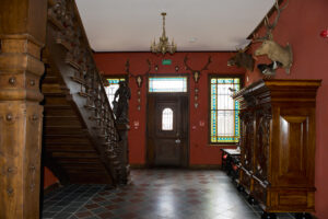korytarz ze schodami drewnianymi prowadzącymi w górę, na ścianach wiszą poroża zwierząt, obok szafa