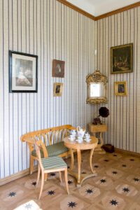 stolik z krzesłem i dekoracyjną ławką, na ścianach obrazy i lustro, obok na stoliku gramofon