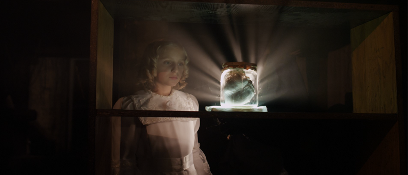 Baner, a na nim: Fragment dzieła Lecha Majewskiego, kadr z wideo, na którym widoczna jest kobieta wpatrująca się w świecący przedmiot, słoik z zawartością