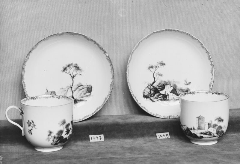Czarno-biała fotografia. Dwie filiżanki ze spodkami, malowane purpurą w motywy pejzażowe, krawędzie złocone, Miśnia, Królewska Manufaktura Porcelany, 2 połowa XVIII w., zakupione razem w 1890 roku.